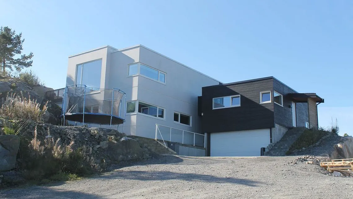 Moderne to-etasjes hus med store vinduer og balkong med glassrekkverk