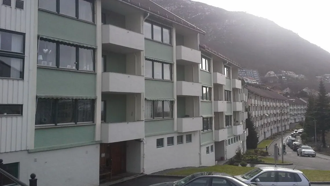 Leilighetsbygg med parkerte biler og fjell i bakgrunnen