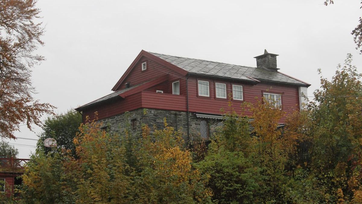 To-etasjes hus med rød fasade og grått tak, omgitt av høstfarget vegetasjon
